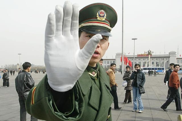 Imagen Ilustrativa: Policía del régimen comunista chino hace un gesto mientras patrulla la Plaza de Tiananmen, 4 de marzo de 2003. (FREDERIC BROWN / AFP vía Getty Images).