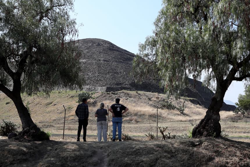 Personas observan la zona arqueológica de Teotihuacán este martes, en San Juan Teotihuacán. Las puertas de la Zona Arqueológica de Teotihuacán permanecen cerradas y los alrededores de la Pirámide de la Luna, donde fueron baleadas varias personas en un tiroteo que dejó dos personas fallecidas, una de nacionalidad canadiense, y trece heridos, no está presente ningún elemento de seguridad, ni local ni federal. (EFE/ Mario Guzmán)