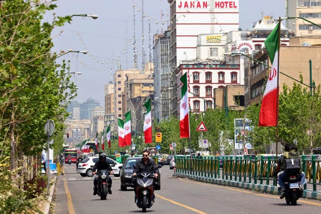 Vehículos y motocicletas circulan por una calle adornada con la bandera iraní en Teherán el 21 de abril de 2026, en medio de un alto el fuego en la región. (Atta Kenare/AFP vía Getty Images).