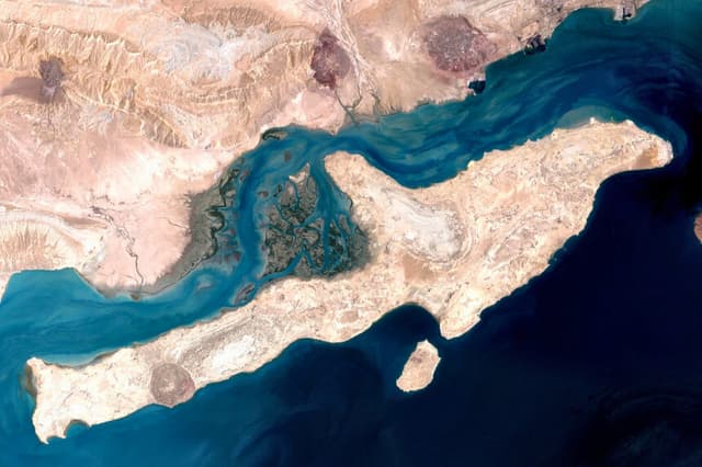 Una imagen de satélite muestra la isla de Qeshm, situada en la desembocadura del estrecho de Ormuz, en el golfo Pérsico, el 23 de agosto de 2000. Los analistas señalan que la toma de la isla —la mayor de Irán en el golfo— podría debilitar la capacidad de Irán para perturbar el tráfico marítimo, aunque tal objetivo resultaría difícil de alcanzar con el actual refuerzo de fuerzas. (NASA/Dominio público/CC0).