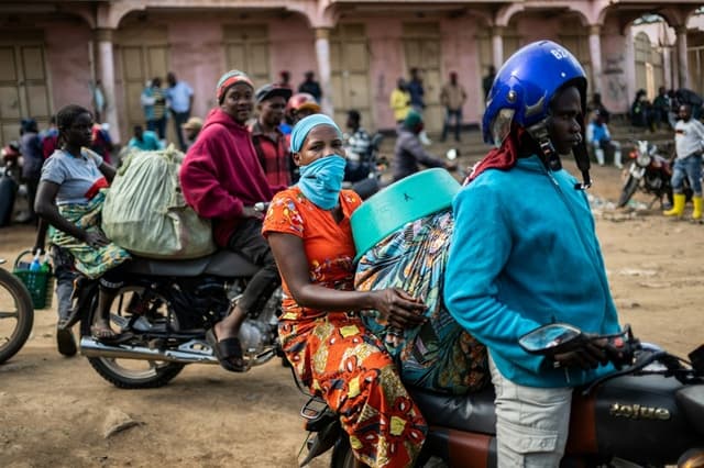 Los conductores de mototaxis y sus pasajeros esperan a la entrada del mercado central mientras los trabajadores de limpieza desinfectan la zona, en el marco de la lucha que la provincia de Ituri sigue librando contra un brote de ébola en Bunia (Congo), el 23 de mayo de 2026. (Moses Sawasawa/AP Photo)