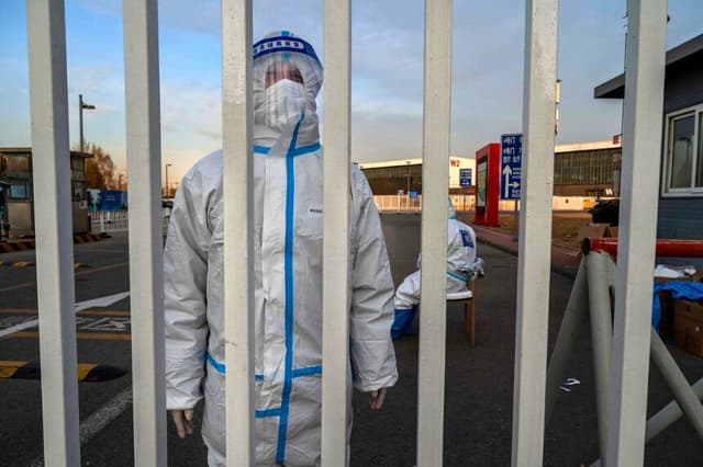 Un trabajador encargado del control de epidemias lleva equipo de protección individual (EPI) para protegerse contra la propagación del COVID-19 mientras vigila la entrada de un centro de cuarentena del gobierno en Beijing, China, el 7 de diciembre de 2022. (Kevin Frayer/Getty Images).
