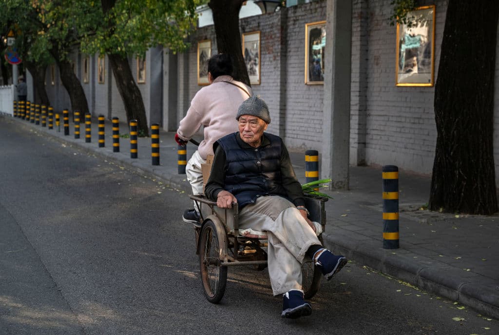 Un anciano viaja en la parte trasera de una bicicleta de tres ruedas en un barrio el 24 de octubre de 2024 en Beijing, China. (Kevin Frayer/Getty Images)
