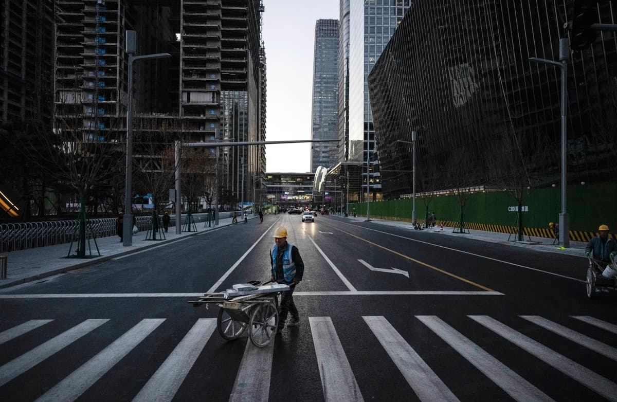 Un trabajador de la construcción empuja una carretilla con materiales al cruzar la calle en el Distrito Central de Negocios de Beijing el 29 de noviembre de 2024. (Kevin Frayer/Getty Images)