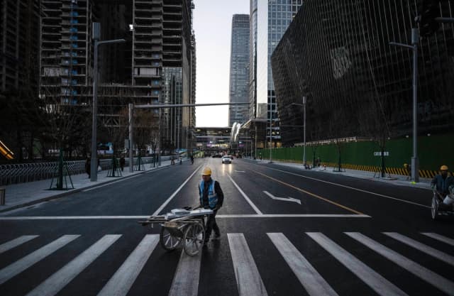 Un trabajador de la construcción empuja una carretilla con materiales al cruzar la calle en el Distrito Central de Negocios de Beijing el 29 de noviembre de 2024. (Kevin Frayer/Getty Images)