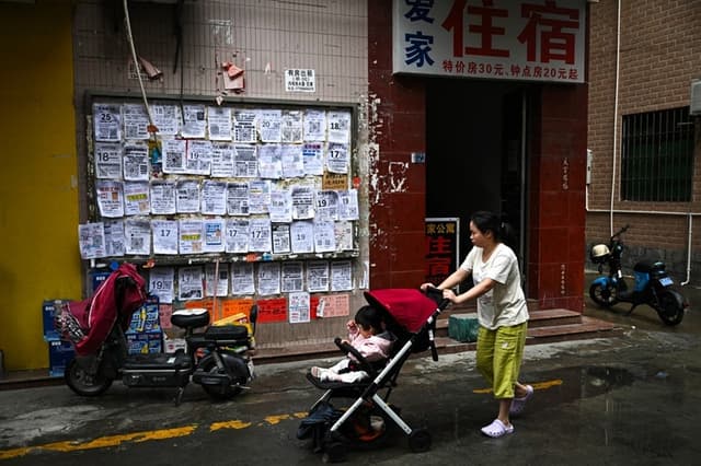 Una mujer empuja un cochecito con un bebé junto a anuncios de empleo exhibidos en un tablero en Foshan, provincia de Guangdong, en China, el 28 de abril de 2026. (Pedro Pardo / AFP vía Getty Images)