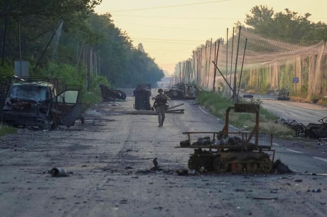 Un militar de la brigada consolidada 'Khyzhak' del Departamento de Policía de Patrulla Ucraniana camina por una carretera cerca de redes antidrones y vehículos militares destruidos mientras participa en una misión para proteger una carretera de drones rusos entre las ciudades del frente de Druzhkivka y Kostiantynivka, en la región de Donetsk, Ucrania, el 24 de junio de 2026. (Anatolii Stepanov/Reuters).