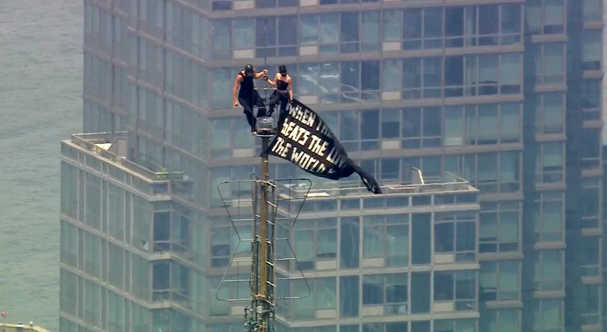 Dos personas se encuentran en la punta de la antena del Empire State Building en Nueva York mientras sostienen una pancarta el 1 de julio de 2026. (WABC-TV vía AP)