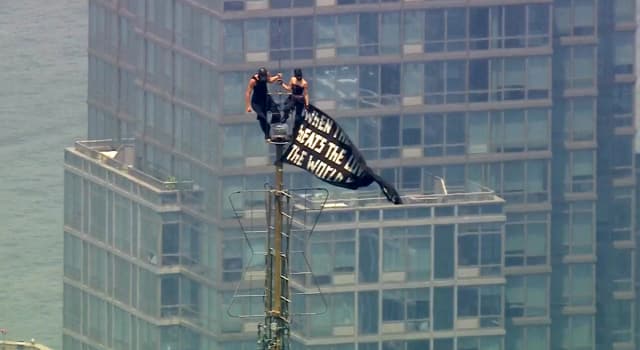 Dos personas se encuentran en la punta de la antena del Empire State Building en Nueva York mientras sostienen una pancarta el 1 de julio de 2026. (WABC-TV vía AP)
