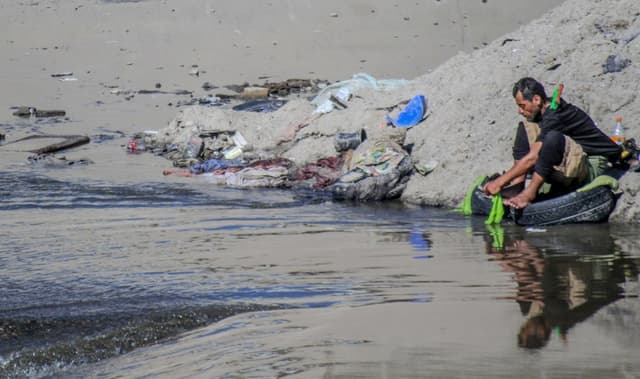 Fotografía de archivo de un migrante en condición de indigencia que lava su ropa en los charcos del río Bravo, que se mantiene sin afluente, en la ciudad de Tijuana, México. (EFE/ Joebeth Terriquez)