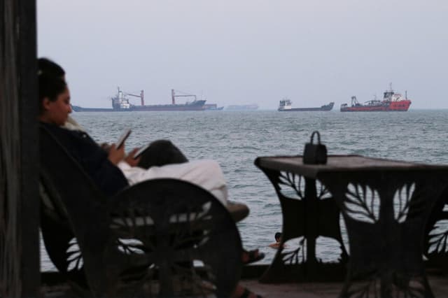 Los residentes consultan sus teléfonos mientras están sentados en una cafetería con vistas a buques comerciales anclados en el estrecho de Ormuz, frente a Bandar Abbas, Irán, el 12 de julio de 2026. (Razieh Poudat/ISNA vía AP).