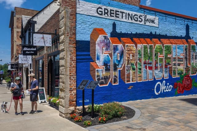 Dos peatones y su perro pasan junto al mural "Saludos desde Springfield, Ohio" en Springfield, Ohio, el 3 de julio de 2026. (Glenn Hartong para The Epoch Times).
