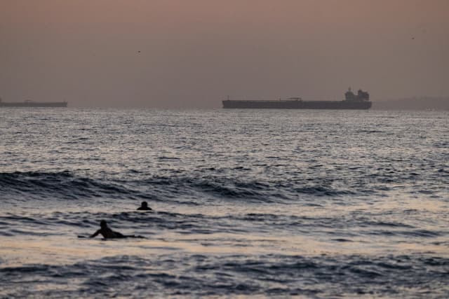 Los bañistas disfrutan del mar con un petrolero de fondo en Huntington Beach, California, el 12 de septiembre de 2024. (John Fredricks/The Epoch Times)