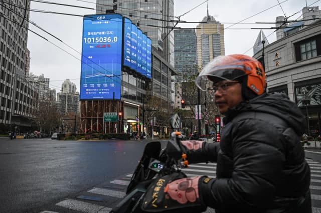 Un hombre pasa en scooter junto a una pantalla que muestra las cifras del producto interior bruto (PIB) en una calle de Shanghái el 19 de enero de 2026. (Jade Gao/AFP vía Getty Images)