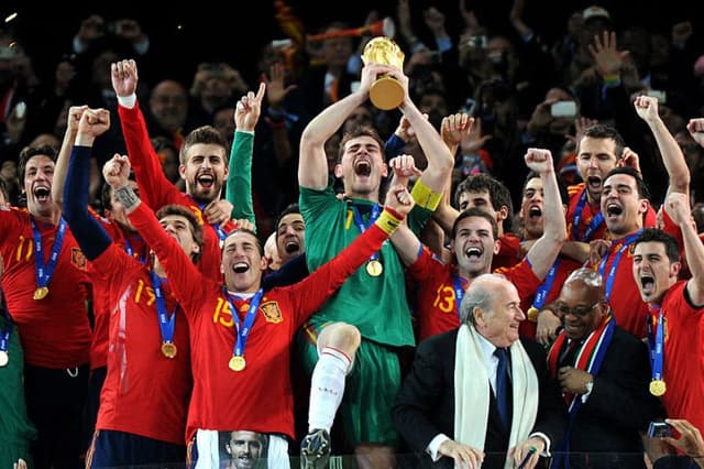 El portero español Iker Casillas (C) levanta el trofeo que le entregaron el presidente de la FIFA, Sepp Blatter (4.º por la derecha), y el presidente de Sudáfrica, Jacob Zuma (3.º por la derecha), mientras los jugadores de la selección española celebran la victoria en la final de la Copa Mundial de Fútbol de 2010 entre Países Bajos y España, el 11 de julio de 2010 en el estadio Soccer City de Soweto, en las afueras de Johannesburgo. (GABRIEL BOUYS / AFP vía Getty Images)