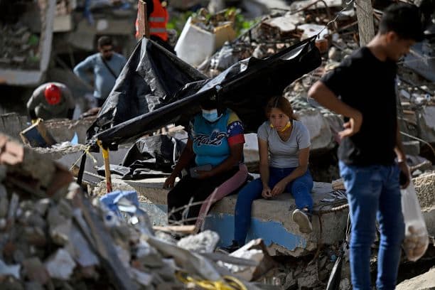 Dos mujeres están sentadas entre los escombros mientras voluntarios y equipos de rescate buscan cuerpos en el lugar donde se derrumbaron varios edificios en Caraballeda, estado de La Guaira, Venezuela, el 16 de julio de 2026. (Federico PARRA / AFP vía Getty Images)