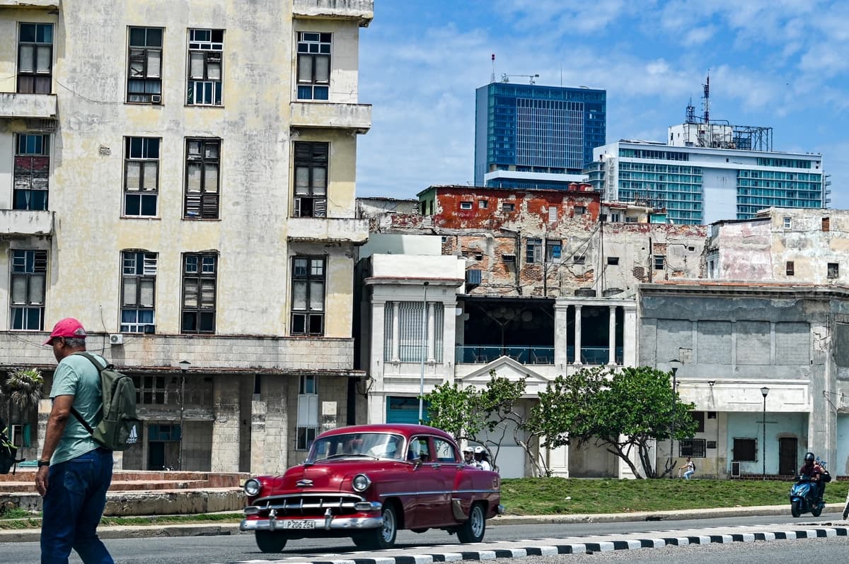 Un hombre camina por una calle mientras pasa un coche clásico, con el hotel Iberostar Selection (C) y el hotel Habana Libre Melia (D) al fondo, en La Habana, el 2 de junio de 2026. (Adalberto Roque/AFP vía Getty Images).