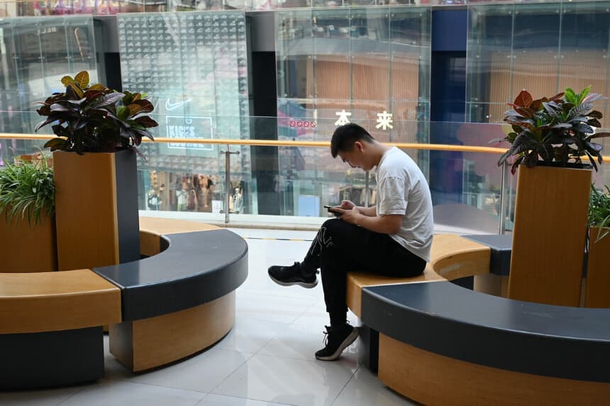 Un hombre revisa su teléfono mientras descansa en un centro comercial de Beijing el 18 de julio de 2023. (Greg Baker/AFP vía Getty Images).