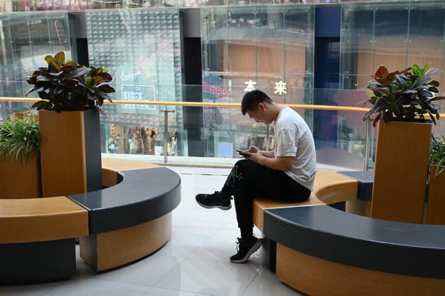 Un hombre revisa su teléfono mientras descansa en un centro comercial de Beijing el 18 de julio de 2023. (Greg Baker/AFP vía Getty Images).
