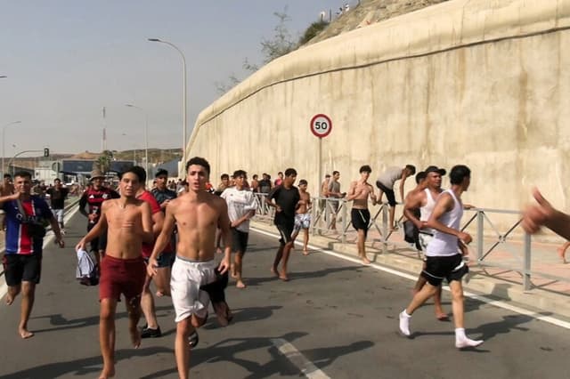 Los migrantes corren y vitorean mientras cruzan a pie desde Marruecos hacia el enclave norteafricano de Ceuta, tras haber nadado desde el lado marroquí y haber desbordado a la policía en el rompeolas de la ciudad, según la Guardia Civil de España, en Ceuta, España, el 30 de julio de 2026, en esta captura de pantalla obtenida de un video difundido. (Faro TV vía Reuters).