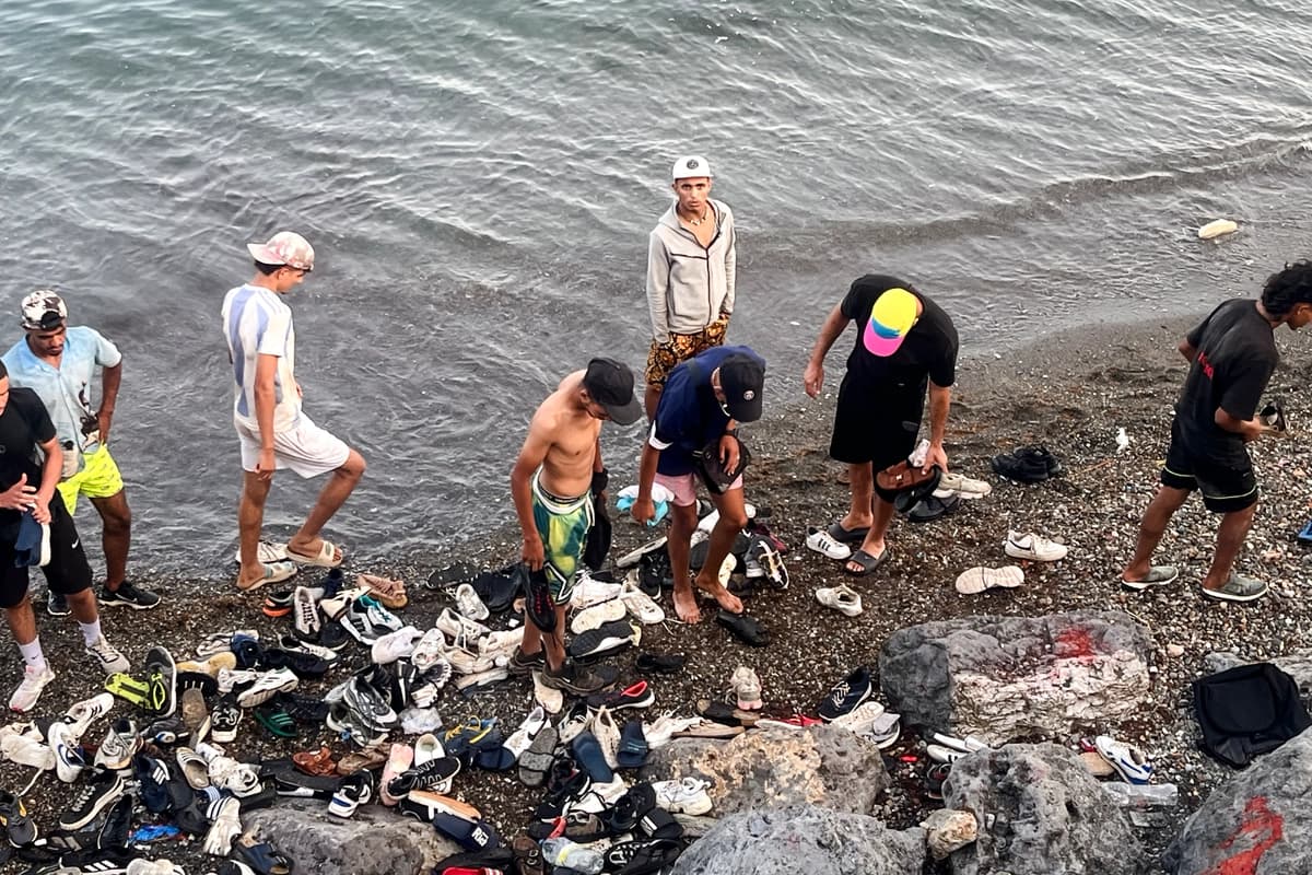 Jóvenes migrantes marroquíes revisan montones de zapatos desechados en una playa rocosa cerca de la Avenida Martínez Catena, en el territorio español de Ceuta, el 31 de julio de 2026, después de cruzar a nado desde Marruecos. (Etienne Fauchaire/The Epoch Times)