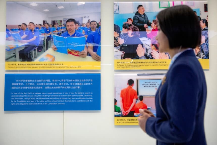 Una guía turística se encuentra cerca de una exhibición que muestra imágenes de personas en lugares descritos como centros de formación profesional en el sur de Xinjiang, durante la Exposición de la Lucha contra el Terrorismo y el Extremismo en Urumqi, en la Región Autónoma Uigur de Xinjiang, China, el 21 de abril de 2021. (Mark Schiefelbein/AP Photo).