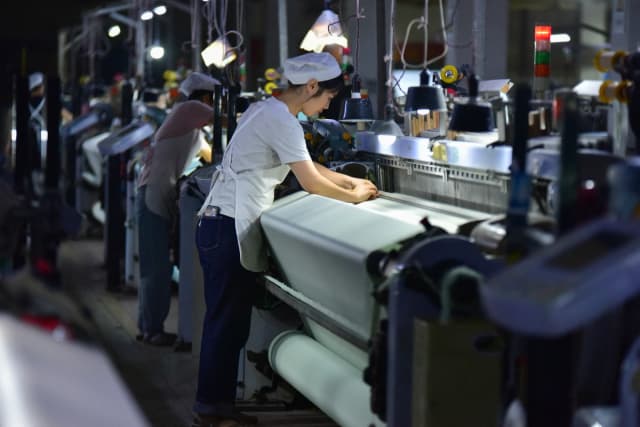 Empleados trabajan en la línea de producción de la empresa Anhui Jingjiu Silk Company en Fuyang, provincia de Anhui, al este de China, el 20 de octubre de 2025. (-STR/AFP vía Getty Images)