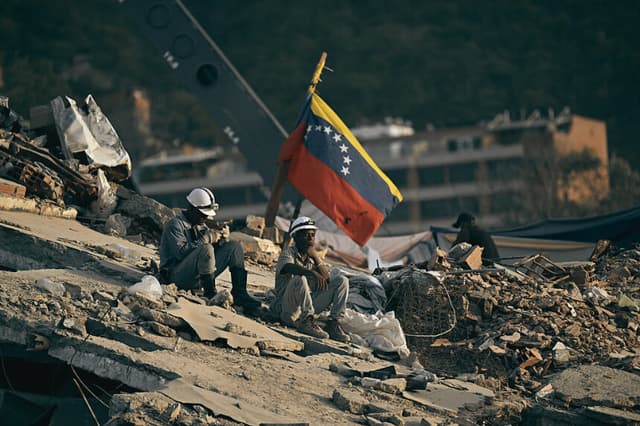 Los voluntarios descansan durante la búsqueda de cuerpos entre los escombros de un edificio en Tanaguarena, La Guaira, Venezuela, el 28 de julio de 2026, un mes después de que un terremoto azotara la zona. (Foto de Juan BARRETO / AFP vía Getty Images)