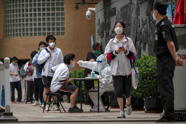 Un trabajador sanitario con traje protector realiza una prueba de ácido nucleico para detectar la COVID-19 a un estudiante tras finalizar el último día del Examen Nacional de Ingreso a la Universidad, también conocido como Gaokao, en un instituto de Beijing el 10 de junio de 2022. (Kevin Frayer/Getty Images).