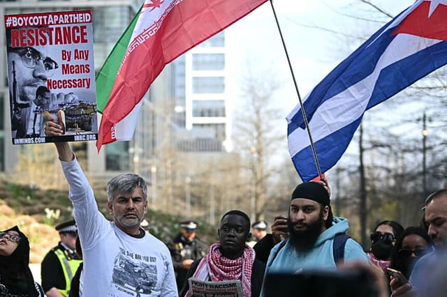 Manifestantes sostienen pancartas y ondean banderas iraníes y cubanas en una protesta masiva de unidad organizada para expresar la oposición al conflicto en el Medio Oriente y a las restricciones que Estados Unidos impuso a Cuba, frente a la embajada de Estados Unidos en el centro de Londres el 22 de marzo de 2026. (JUSTIN TALLIS / AFP vía Getty Images)
