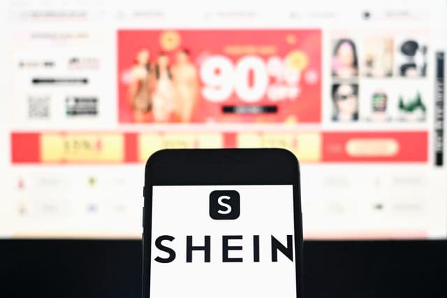 El logotipo de la empresa de comercio electrónico de moda Shein se muestra en un smartphone con la página web de la empresa al fondo en una fotografía tomada en Bangkok, Tailandia, el 6 de diciembre de 2024. (Manan Vatsyayana/AFP vía Getty Images).