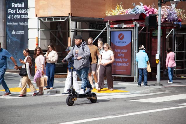 Un hombre cruza una intersección cerca de Union Square en San Francisco en un patinete eléctrico el 7 de agosto de 2026. (Lear Zhou/The Epoch Times).