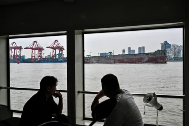 Varias personas se sientan en un ferry que cruza el río Huangpu junto a grúas en las terminales de contenedores de Shanghái, en el muelle de Zhanghuabang, Shanghái, China, el 7 de mayo de 2026. (Hector Retamal / AFP vía Getty Images).