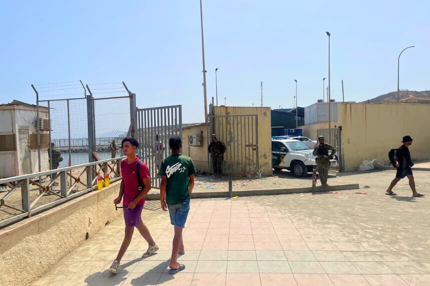 Migrantes marroquíes caminan cerca de la frontera española con Marruecos mientras oficiales y personal militar de la Guardia Civil se encuentran junto a un vehículo de la Guardia Civil en Ceuta, España, el 1 de agosto de 2026. (Etienne Fauchaire/The Epoch Times).