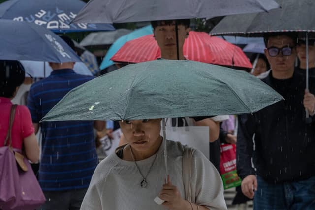 Los transeúntes llevan paraguas mientras caminan por la calle durante una tormenta provocada por el tifón Dolphin en Pekín, el 12 de agosto de 2026. (Kevin Frayer/Getty Images).