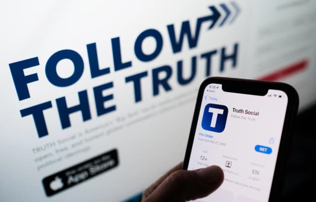 Esta foto ilustrativa muestra a una persona buscando Truth Social en la tienda de aplicaciones de su teléfono inteligente, con su sitio web en la pantalla de una computadora al fondo, en Los Ángeles el 20 de octubre de 2021. (Chris Delmas/AFP vía Getty Images).