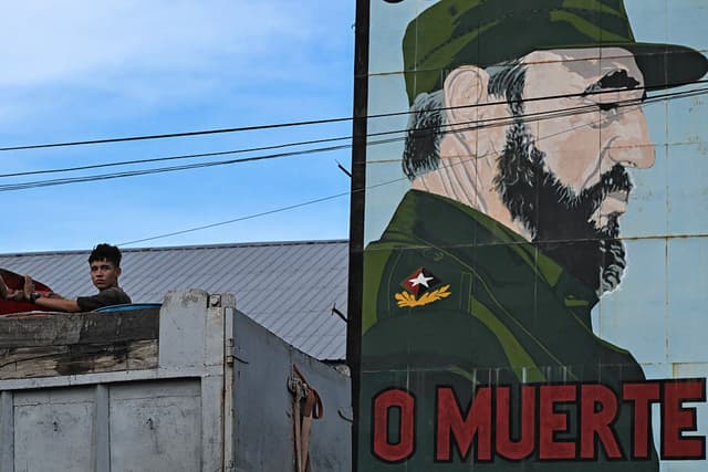 Un joven aparece junto a un retrato del fallecido líder cubano Fidel Castro (1926-2016) en La Habana, el 10 de agosto de 2026. El 13 de agosto de 2026 se conmemora el centenario del nacimiento de Fidel Castro, el líder que dirigió la Revolución Cubana durante casi medio siglo, mientras muchos de sus seguidores más leales se enfrentan a una de las peores crisis de las últimas décadas, marcada por apagones, escasez e incertidumbre. (YAMIL LAGE / AFP vía Getty Images)