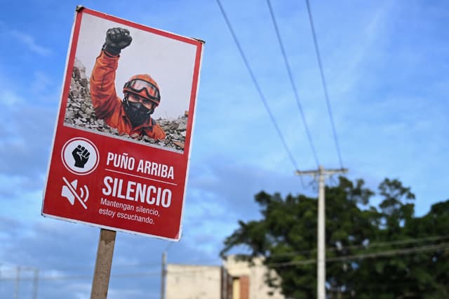 Un rescatista sostiene un letrero que dice "Silencio, estoy escuchando" cerca de edificios derrumbados tras un terremoto en Cali, Colombia, el 14 de agosto de 2026. (Raúl ARBOLEDA / AFP vía Getty Images)