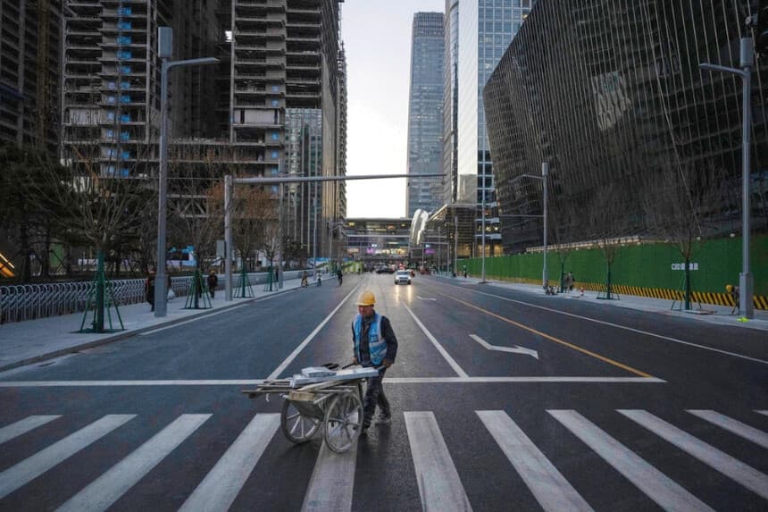 Un trabajador de la construcción empuja una carretilla con materiales al cruzar la calle en el Distrito Central de Negocios de Beijing el 29 de noviembre de 2024. (Kevin Frayer/Getty Images).