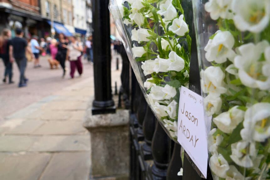 La gente pasa junto a homenajes florales para recordar a Jason Arday, colgados en las barandillas frente a la Casa del Senado en la Universidad de Cambridge, en Cambridge, al este de Inglaterra, el 15 de agosto de 2026. (Justine Gerardy/AFP vía Getty Images).