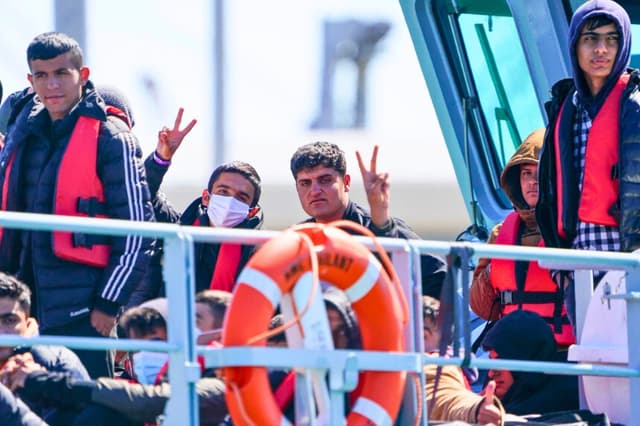 Los inmigrantes ilegales que cruzaron el Canal de la Mancha desde Francia hacen signos de V en el barco Valiant de la Fuerza Fronteriza del Reino Unido al llegar al puerto de Dover, Inglaterra, el 14 de junio de 2022. (Chris Eades /Getty Images).