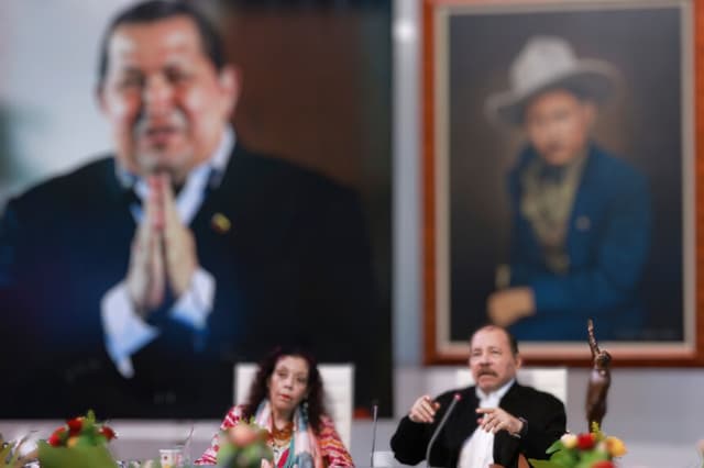 Esta imagen de archivo difundida por la Presidencia de Nicaragua muestra a Daniel Ortega (a la derecha) hablando junto a su esposa y vicepresidenta, Rosario Murillo, y frente a una foto gigante del fallecido expresidente venezolano Hugo Chávez (a la izquierda, de espaldas) durante la XI Cumbre Extraordinaria (virtual) de la ALBA-TCP, celebrada en Managua el 26 de agosto de 2024. (César PÉREZ / Presidencia de Nicaragua / AFP)