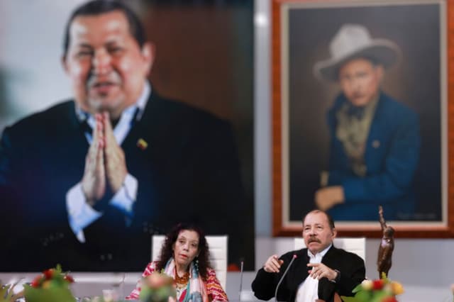 Esta imagen de archivo difundida por la Presidencia de Nicaragua muestra a Daniel Ortega (a la derecha) hablando junto a su esposa y vicepresidenta, Rosario Murillo, y frente a una foto gigante del fallecido expresidente venezolano Hugo Chávez (a la izquierda, de espaldas) durante la XI Cumbre Extraordinaria (virtual) de la ALBA-TCP, celebrada en Managua el 26 de agosto de 2024. (César PÉREZ / Presidencia de Nicaragua / AFP)