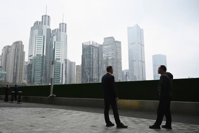 Dos hombres charlan frente a edificios de oficinas en el distrito central de negocios de Beijing el 4 de marzo de 2026. (Greg Baker/AFP vía Getty Images).