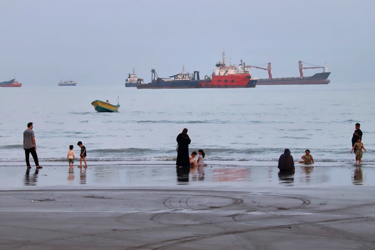 La gente pasa tiempo en una playa mientras barcos comerciales anclan en el Estrecho de Ormuz frente a Bandar Abbas, Irán, el 5 de agosto de 2026. (Amirhosein Khorgooi/ISNA vía AP).