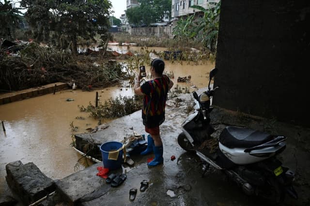Una mujer filma daños fuera de una hilera de casas que se inundaron hasta la segunda planta cuando un embalse se derrumbó cerca de Gantang, en la región suroeste de Guangxi, China, el 9 de julio de 2026. (Greg Baker/AFP vía Getty Images).