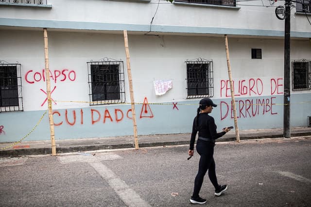 Una mujer pasa junto a un muro en el que se lee una advertencia de riesgo de derrumbe, 14 días después del terremoto de magnitud 7.4 ocurrido en Pereira, Colombia, el 24 de agosto de 2026. (ESTEBAN VEGA LA-ROTTA / AFP vía Getty Images)