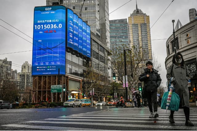 Varias personas pasan junto a una pantalla con cifras del PIB en Shanghái el 19 de enero de 2026. (Jade Gao/AFP vía Getty Images).