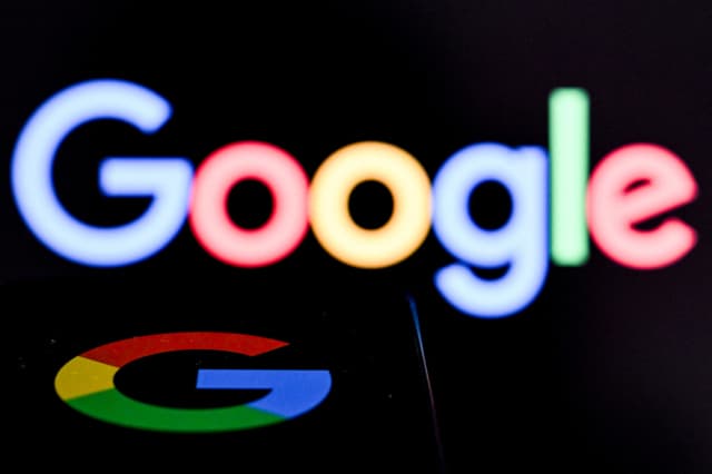 Una fotografía tomada el 19 de mayo de 2026 muestra a Google, la empresa multinacional estadounidense de tecnología y servicios relacionados con internet, en la pantalla de un teléfono inteligente (abajo) frente al logotipo de Google en la pantalla de una computadora portátil en Fráncfort del Meno, en el oeste de Alemania. (Kirill KUDRYAVTSEV / AFP via Getty Images)