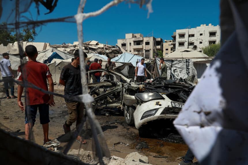 Residentes caminan por una zona dañada junto a un coche destruido tras los ataques israelíes en la ciudad de Gaza el 1 de septiembre de 2026. (Eyad Azam/Middle East Images/AFP vía Getty Images).